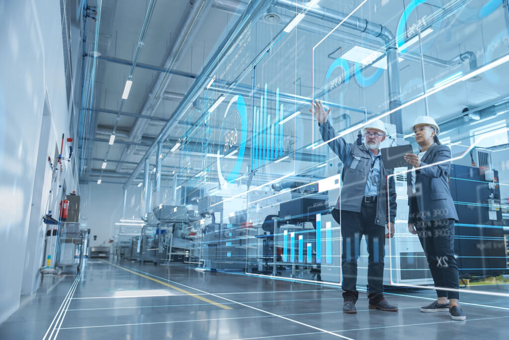 digitale Services Ingenieure stehen in einer Industriehalle mit Maschinen und bedienen ein holographisches Display als Zeichen für Digitalisierung